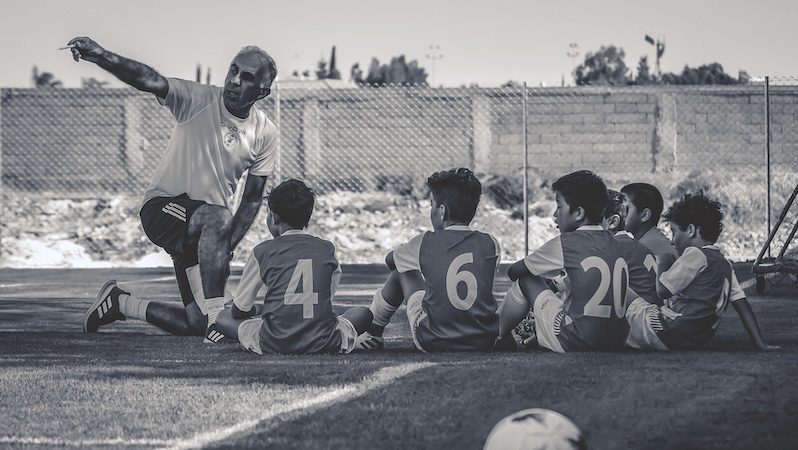 Trainer erklärt jungen Fußballern eine Taktik auf dem Spielfeld – Symbolbild für Coaching und strukturiertes Training
